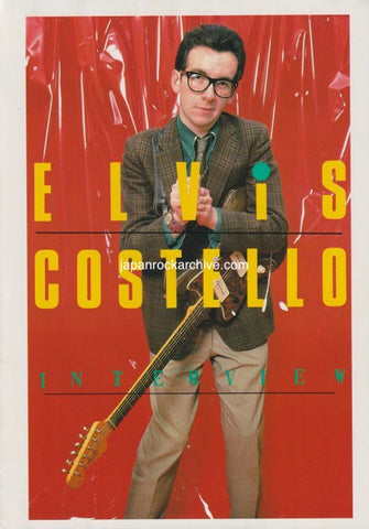Elvis Costello in suit jacket holding a guitar with 'Elvis Costello' text on a red background