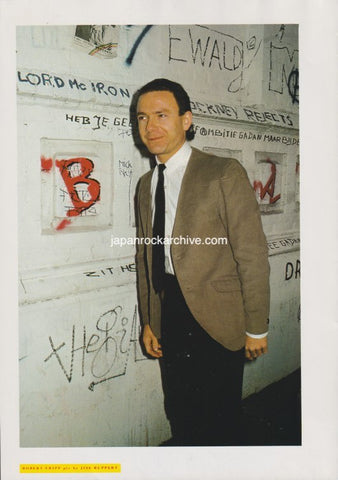 robert fripp of king crimson in a suit standing in front of a wall with graffiti