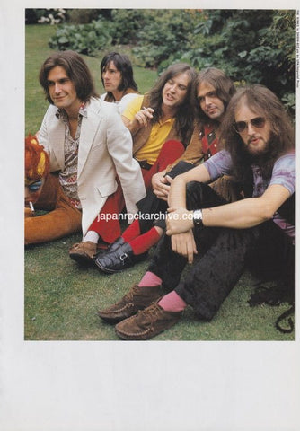 The Kinks with long hair sitting on grass, wearing colorful clothing.
