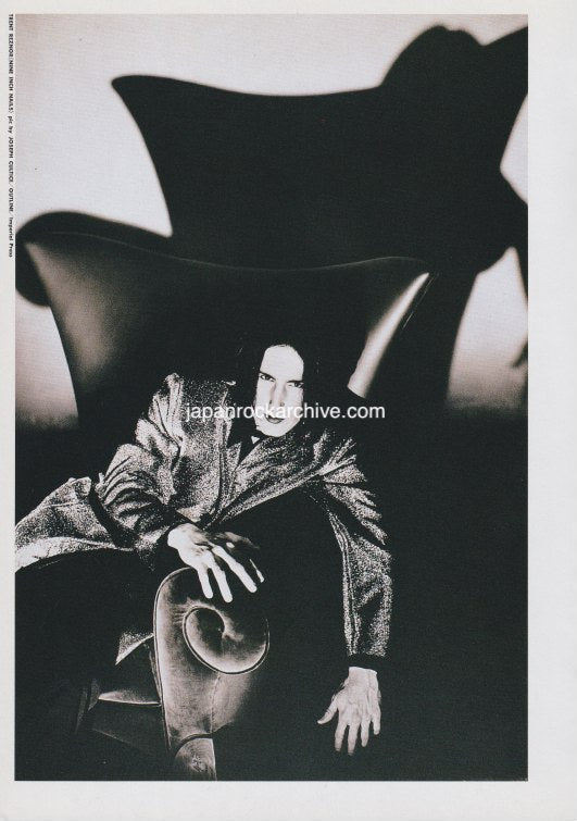 Black and white photograph of trent reznor of nine inch nails in a dramatic pose sitting in a huge chair