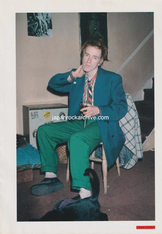 John Lydon of PIL sitting on a chair with a drink in hand, wearing a green suit and tie, from a Japanese music press cutting.