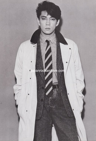 ryuichi sakamoto of YMO wearing a coat, tie, and vest against a plain background