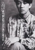 ryuichi sakamoto of ymo wearing a flower patterned shirt sitting.