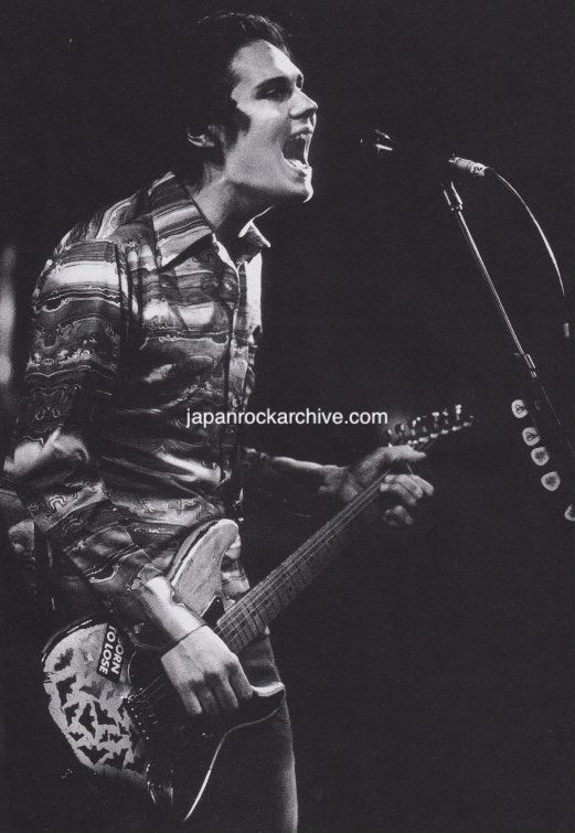 Billy Corgan of Smashing Pumpkins on stage playing guitar and singing into a microphone.