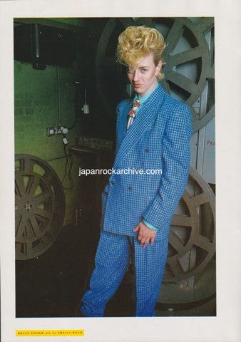 brian setzer of stray cats wearing a blue checkered suit standing in front of large wheels.