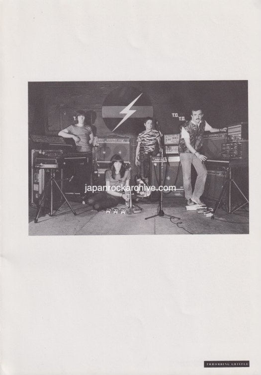 Black and white photo of Throbbing Gristle on stage with equipment and their logo in the background.
